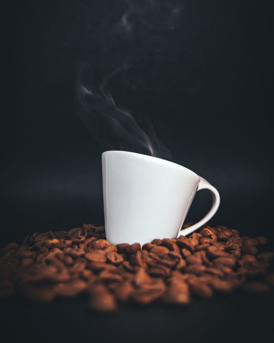 Tazzina bianca fumante appoggiata su chicchi di caffè tostati